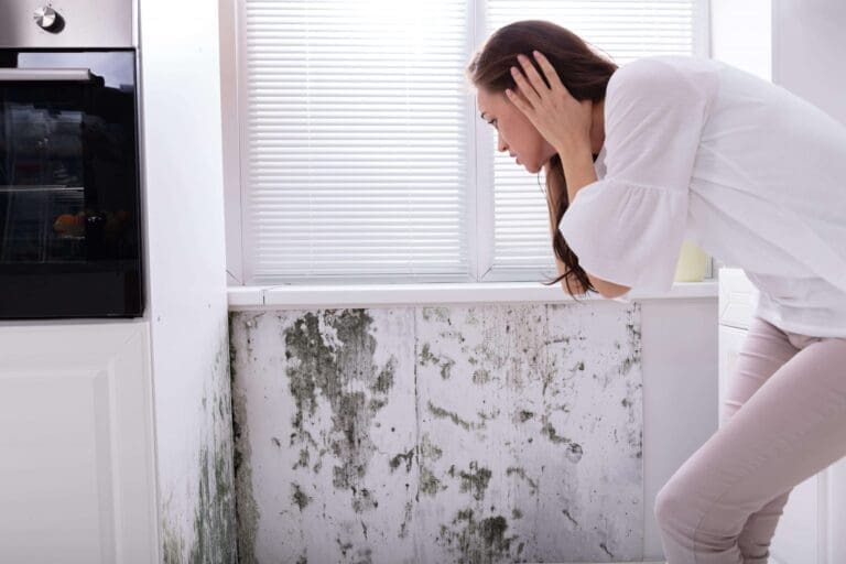 woman looking worried seeing mold on wall under a window.